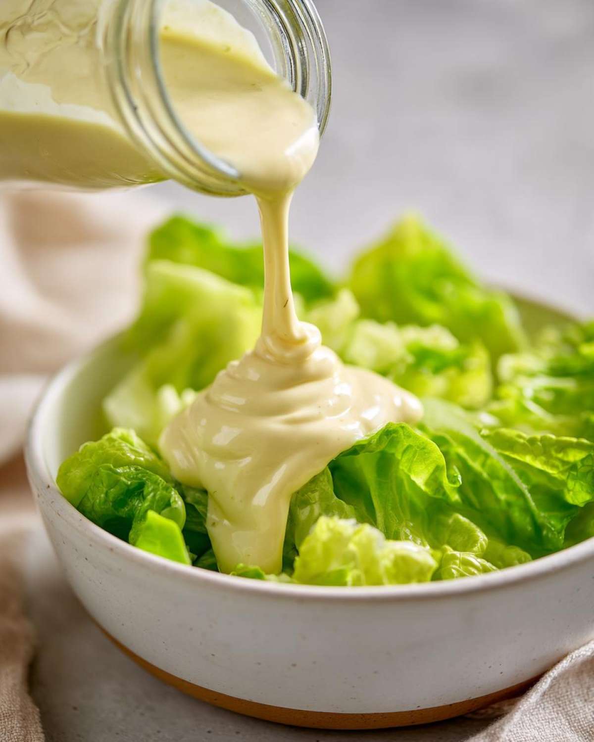 Thick, creamy Copycat Olive Garden Salad Dressing being poured from a jar onto fresh green lettuce in a white bowl.
