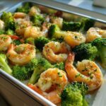 Close-up of cooked shrimp and bright green broccoli florets coated in garlic butter on a sheet pan.