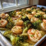 Close-up of Sheet Pan Garlic Butter Shrimp and Broccoli seasoned with herbs on a metal baking sheet.