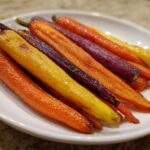 Close-up of glossy Sheet Pan Roasted Rainbow Carrots with Honey, featuring orange, yellow, and purple varieties, served on a white plate.