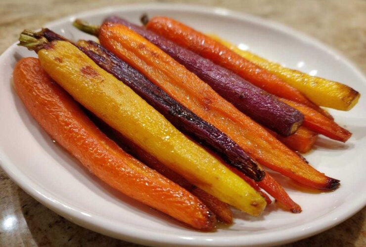 Close-up of glossy Sheet Pan Roasted Rainbow Carrots with Honey, featuring orange, yellow, and purple varieties, served on a white plate.
