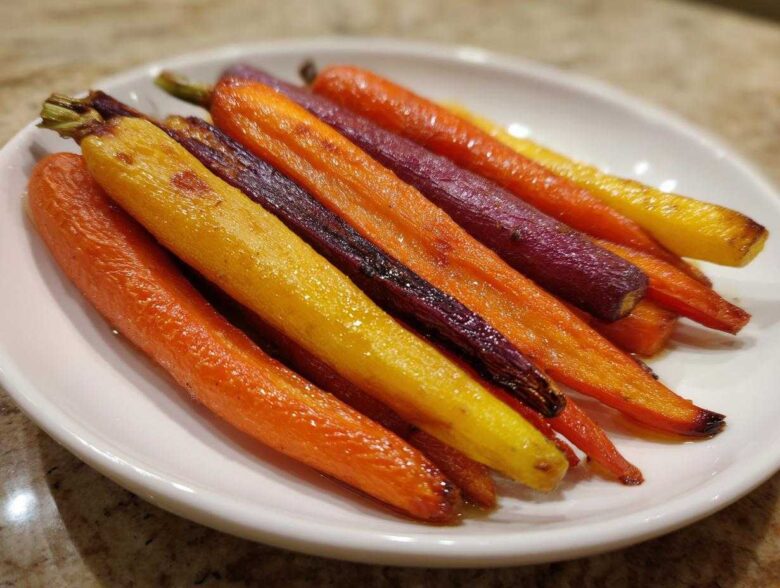 Close-up of glossy Sheet Pan Roasted Rainbow Carrots with Honey, featuring orange, yellow, and purple varieties, served on a white plate.