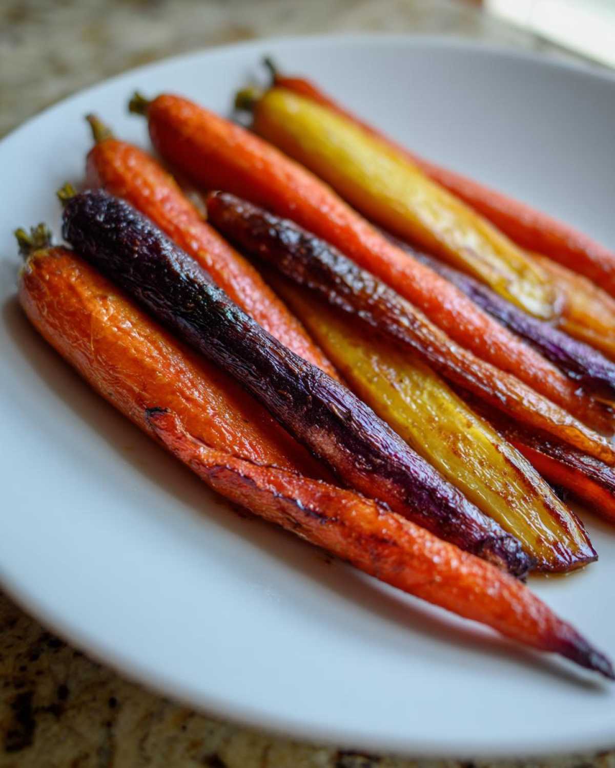 Close-up of glossy, roasted Sheet Pan Roasted Rainbow Carrots with Honey on a white plate.