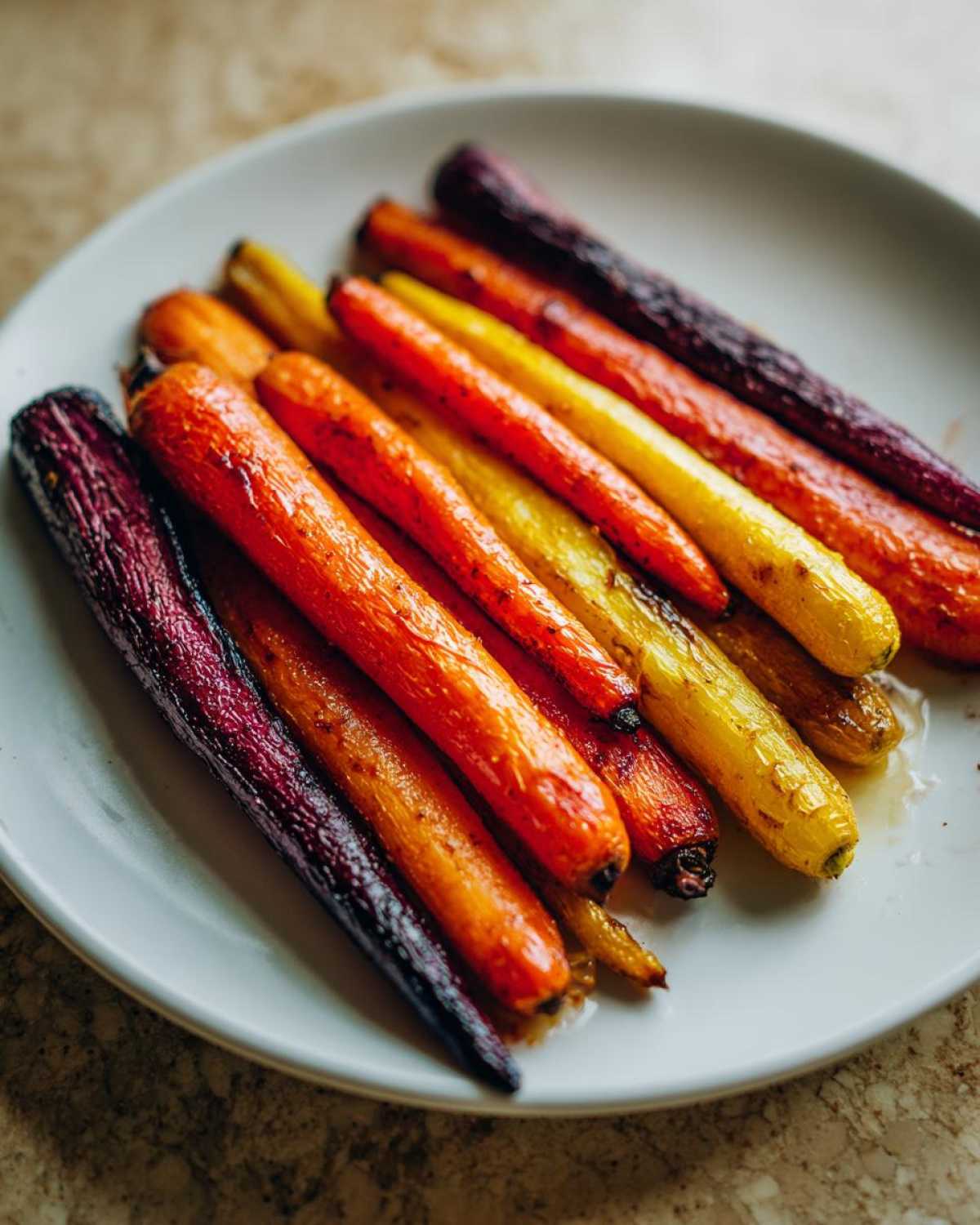 Close-up of roasted Sheet Pan Roasted Rainbow Carrots with Honey, showing purple, orange, and yellow carrots on a white plate.