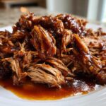 Close-up of tender, shredded Slow Cooker Honey Garlic Pulled Pork coated in a rich, glossy sauce on a white plate.