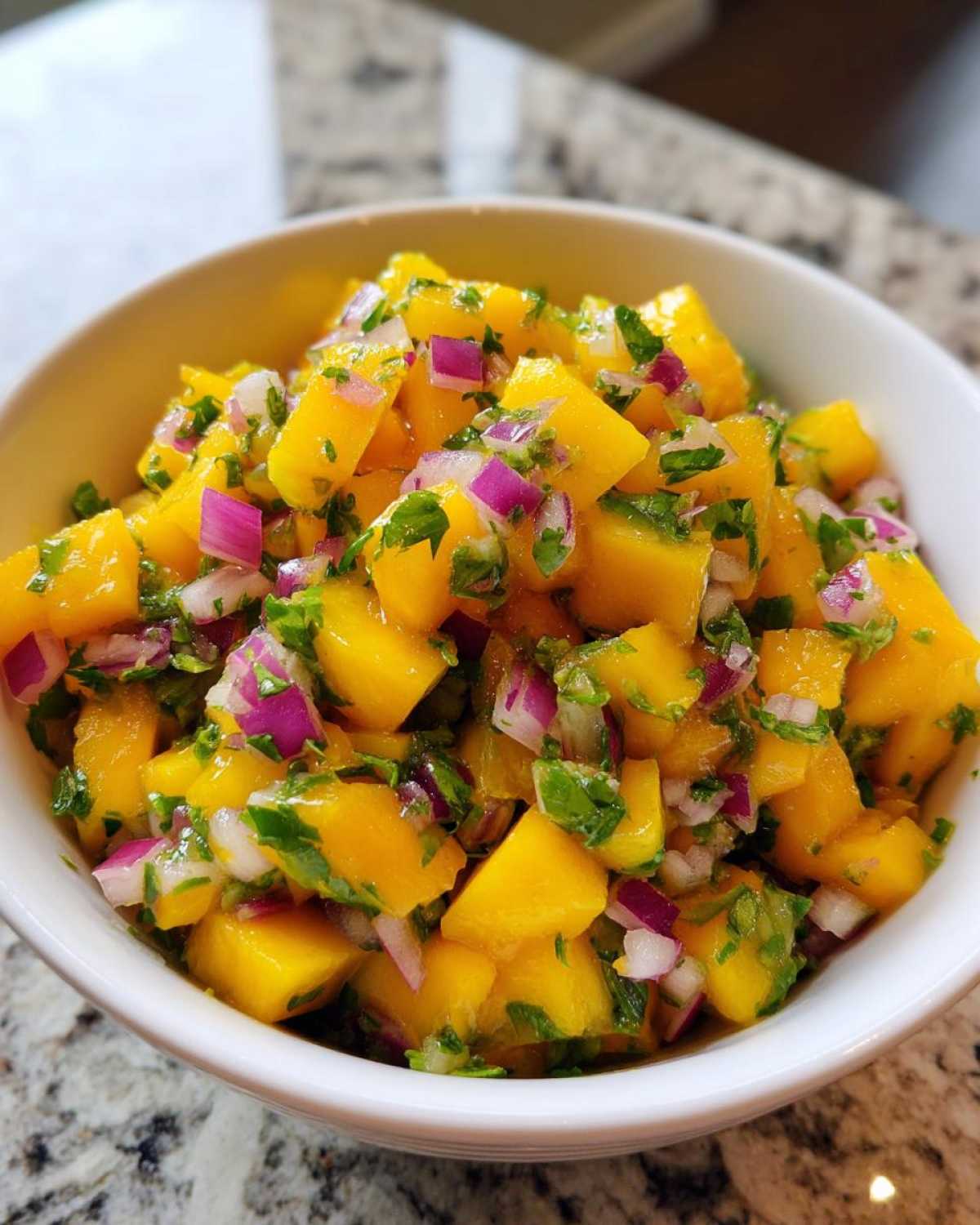 Close-up of a white bowl filled with freshly made Spicy Mango Salsa, showing diced mango, red onion, and cilantro.
