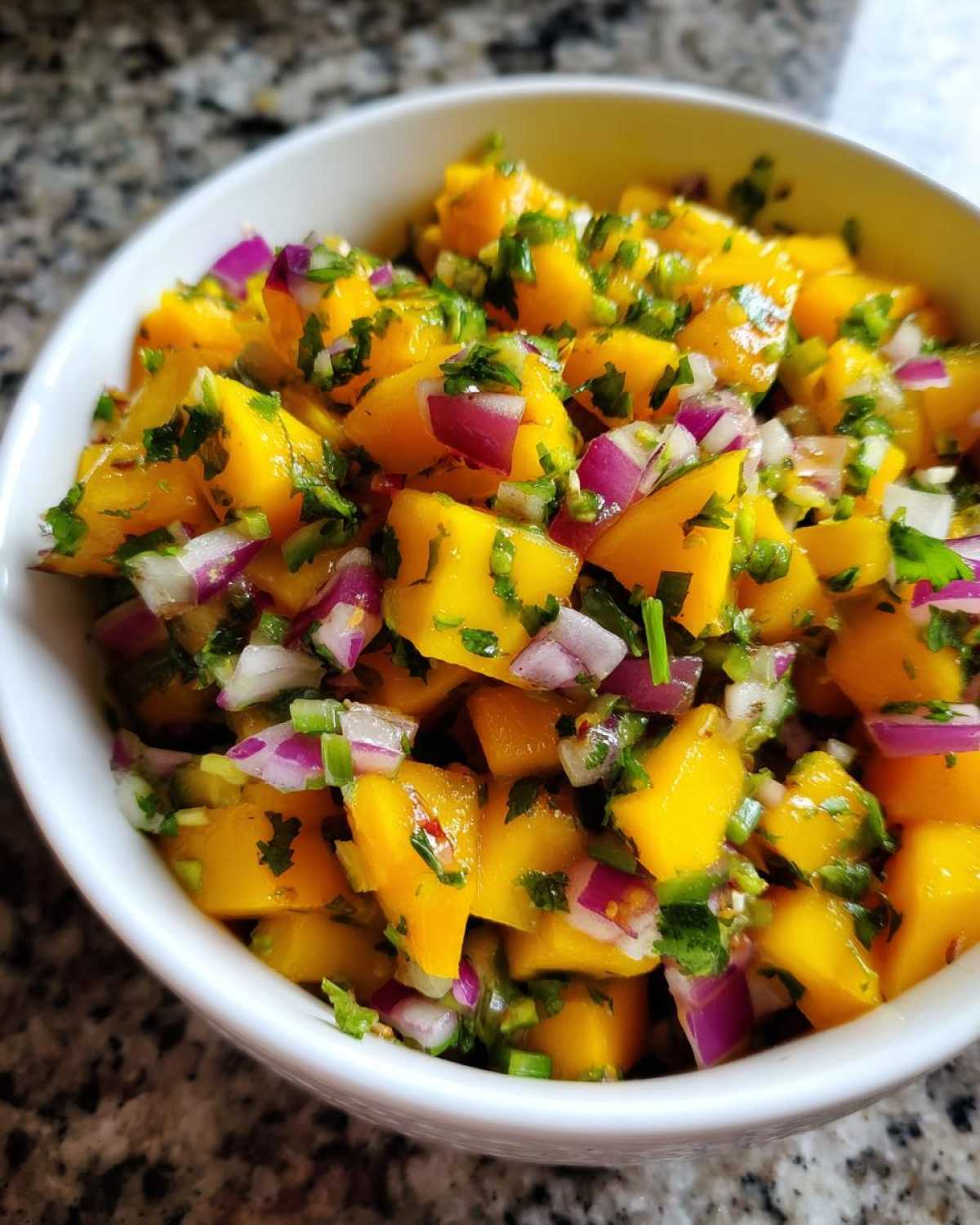 Close-up of diced mango, red onion, and cilantro in a white bowl, showcasing the fresh Spicy Mango Salsa.