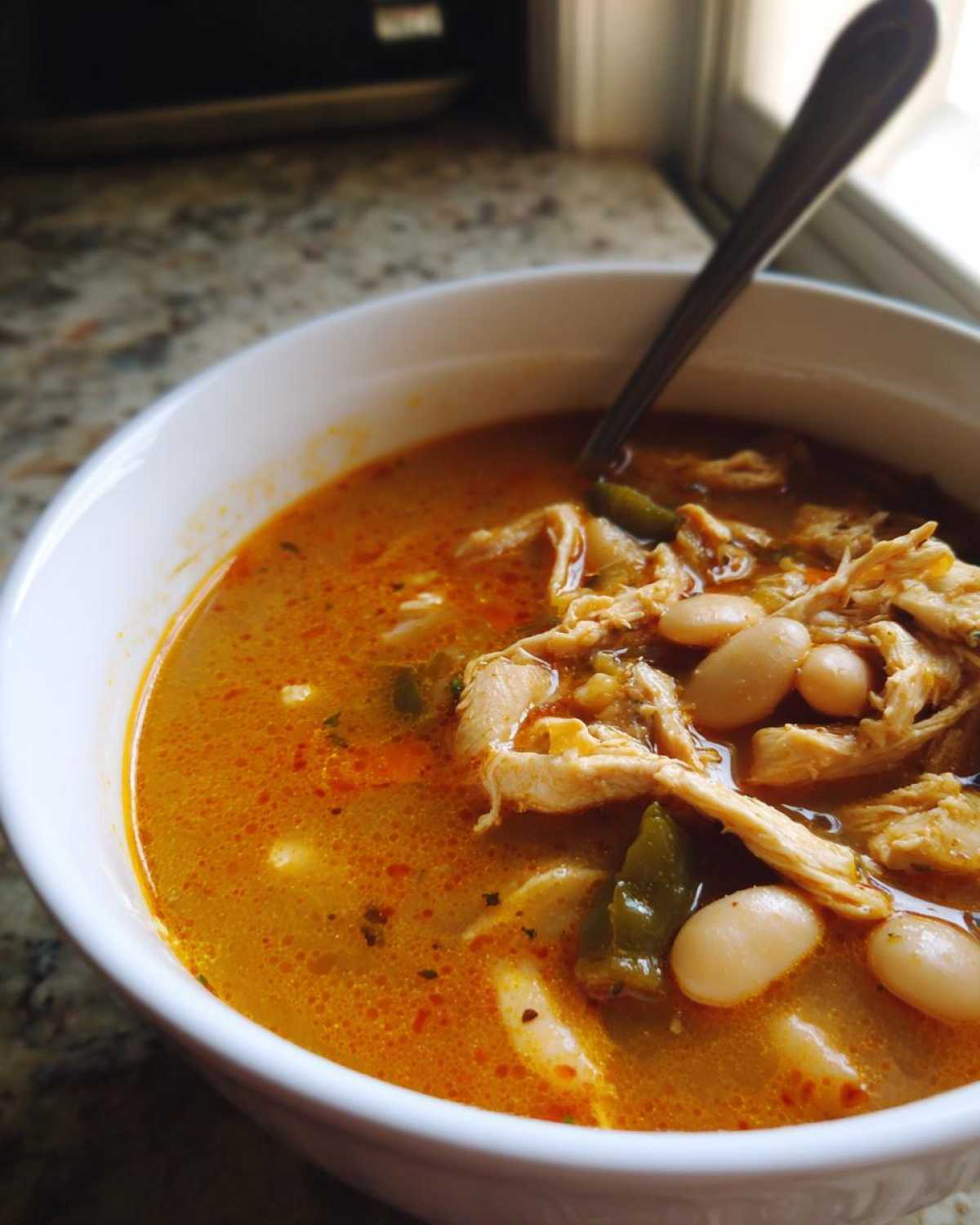 Close-up of a white bowl filled with Spicy Turkey White Bean Chili, showing shredded turkey, white beans, and orange broth.
