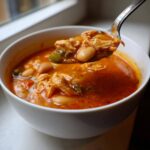 A spoonful of Spicy Turkey White Bean Chili lifted from a white bowl, showing shredded turkey and white beans in a rich broth.
