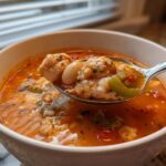 A spoonful of Spicy Turkey White Bean Chili featuring turkey, white beans, and peppers being lifted from a white bowl.