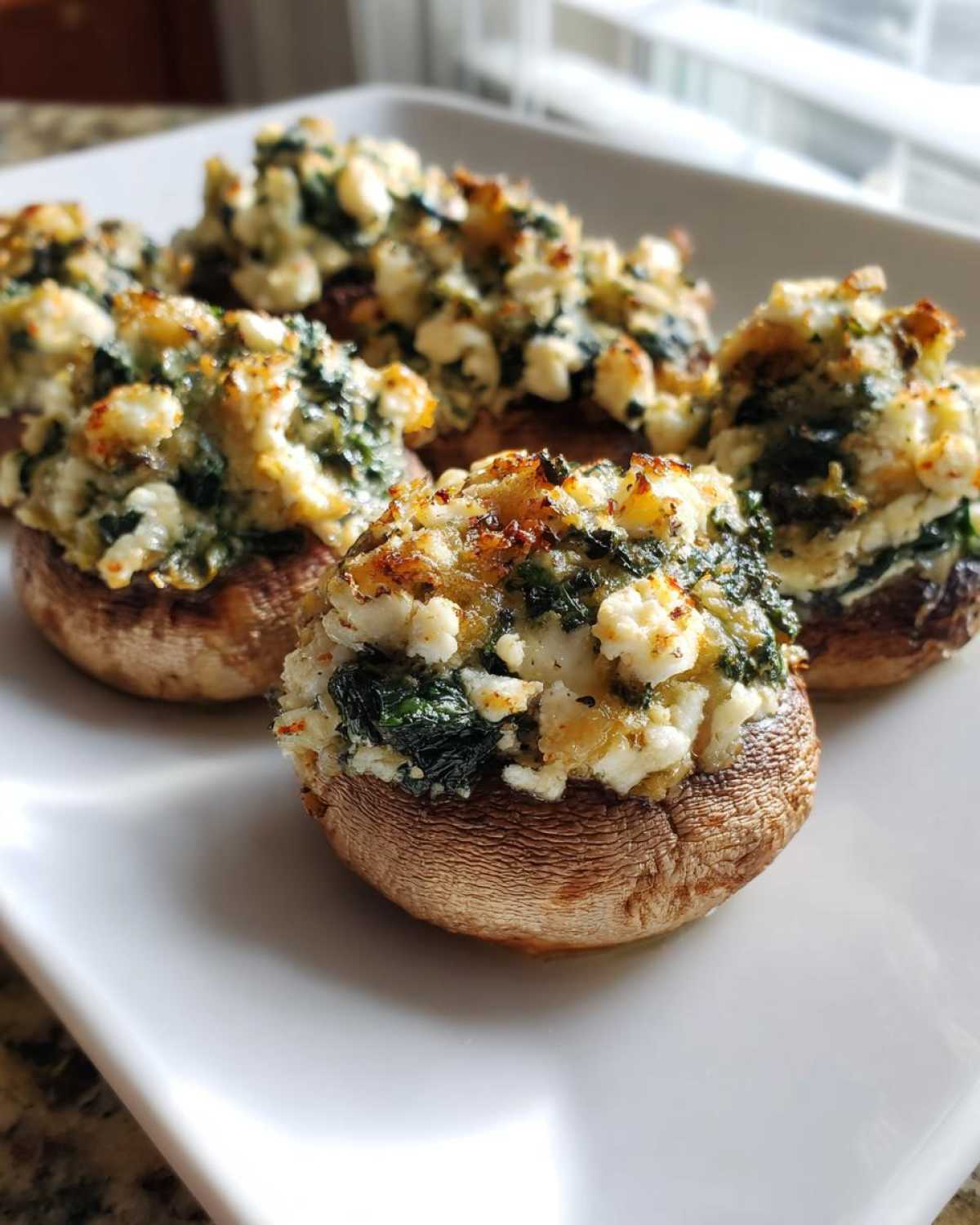 Close-up of baked Spinach and Feta Stuffed Mushrooms piled high with filling on a white serving platter.
