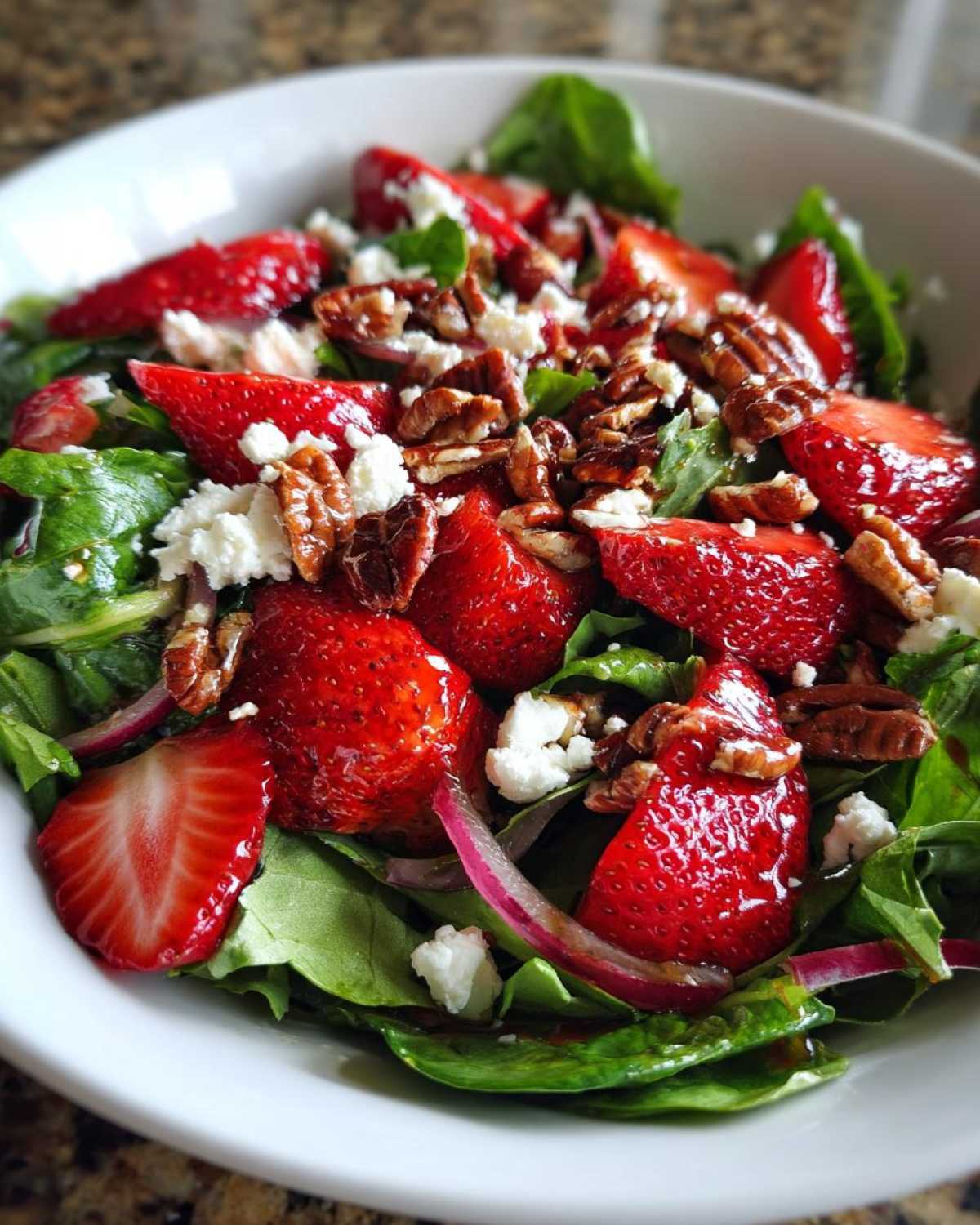 Close-up of a vibrant Spring Mix Salad with Strawberries and Goat Cheese, topped with pecans and red onion slices.