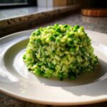 A molded serving of bright green Spring Pea and Mint Risotto topped with whole peas on a white plate.