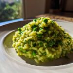 A close-up of creamy Spring Pea and Mint Risotto mounded on a white plate, brightly lit by natural light.