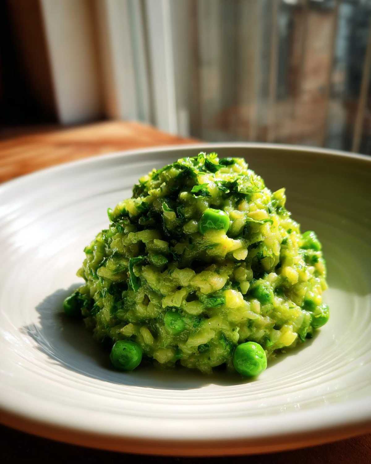 A mound of bright green Spring Pea and Mint Risotto served in a light bowl, highlighted by natural light.