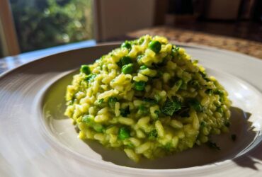 A close-up of creamy Spring Pea and Mint Risotto mounded on a white plate, brightly lit by natural light.