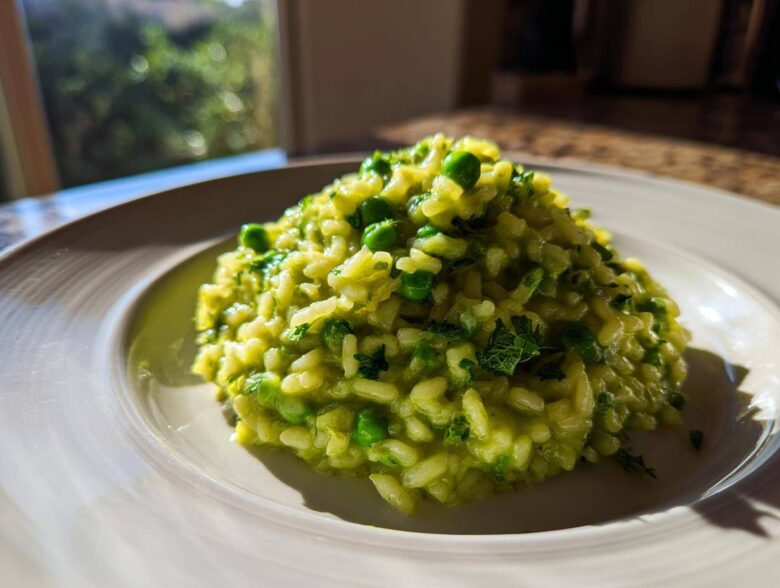 A close-up of creamy Spring Pea and Mint Risotto mounded on a white plate, brightly lit by natural light.