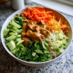 Close-up of a fresh Spring Roll Bowl with Peanut Sauce, featuring rice noodles, cucumbers, carrots, mint, and rich peanut sauce.