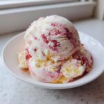 Two scoops of creamy Strawberry Banana Ice Cream swirled with pink fruit puree in a small white bowl.