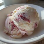 Two scoops of creamy white Strawberry Banana Ice Cream swirled with bright pink strawberry pieces in a white bowl.