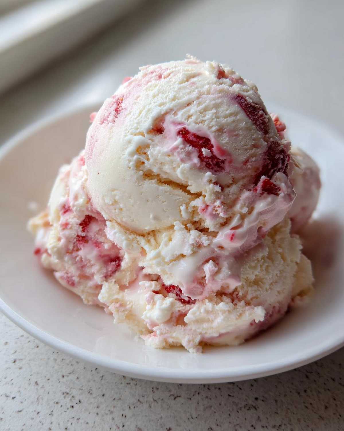 Close-up of creamy scoops of Strawberry Banana Ice Cream swirled with bright pink strawberry pieces.