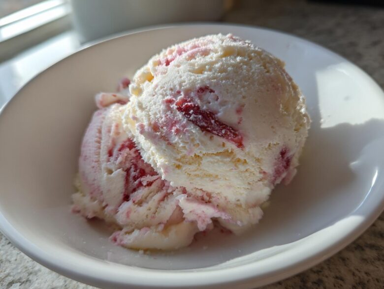 Two scoops of creamy white Strawberry Banana Ice Cream swirled with bright pink strawberry pieces in a white bowl.