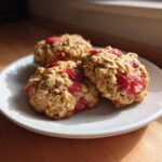 Three freshly baked Strawberry Oatmeal Breakfast Cookies studded with bright red fruit pieces, resting on a white plate.