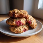A stack of four golden-brown Strawberry Oatmeal Breakfast Cookies with visible bright red berry filling on a light gray plate.
