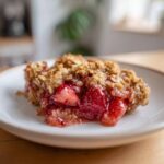 A close-up of a warm serving of Strawberry Rhubarb Crisp showing the bubbling strawberry filling and crunchy oat topping.