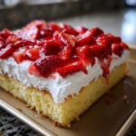 Close-up of a moist slice of Strawberry Shortcake Sheet Cake topped with thick whipped cream and glazed strawberries.