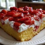 A close-up of a moist slice of Strawberry Shortcake Sheet Cake with whipped cream and fresh glazed strawberries.