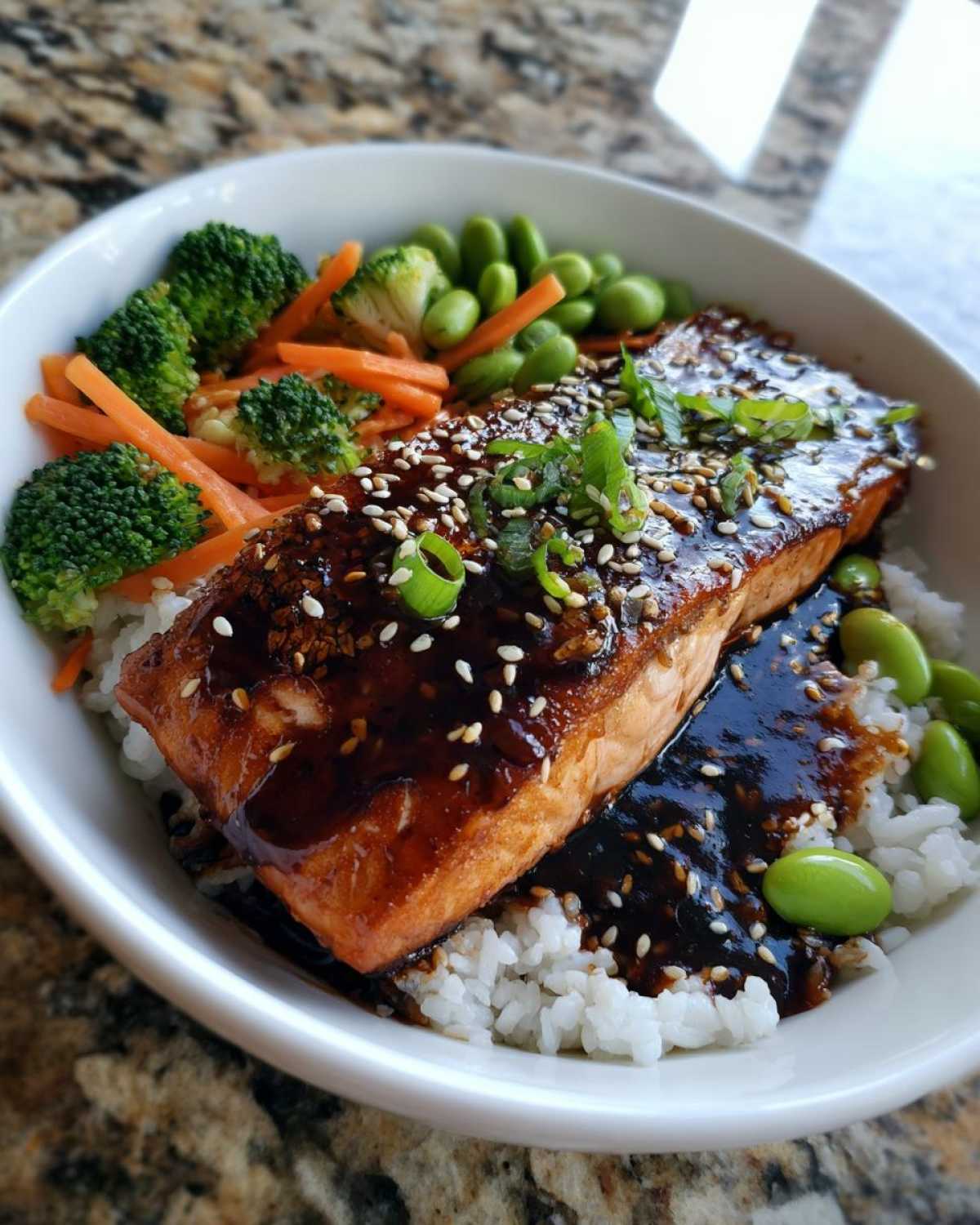 Close-up of a Teriyaki Salmon Rice Bowls featuring glazed salmon over white rice with broccoli, carrots, and edamame.