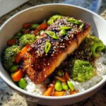 A close-up of a perfectly cooked piece of salmon glazed with teriyaki sauce and sesame seeds in Teriyaki Salmon Rice Bowls.