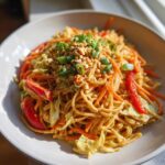 A bowl of creamy Thai Peanut Noodles with Crunchy Veggies, topped with chopped peanuts and green onions.