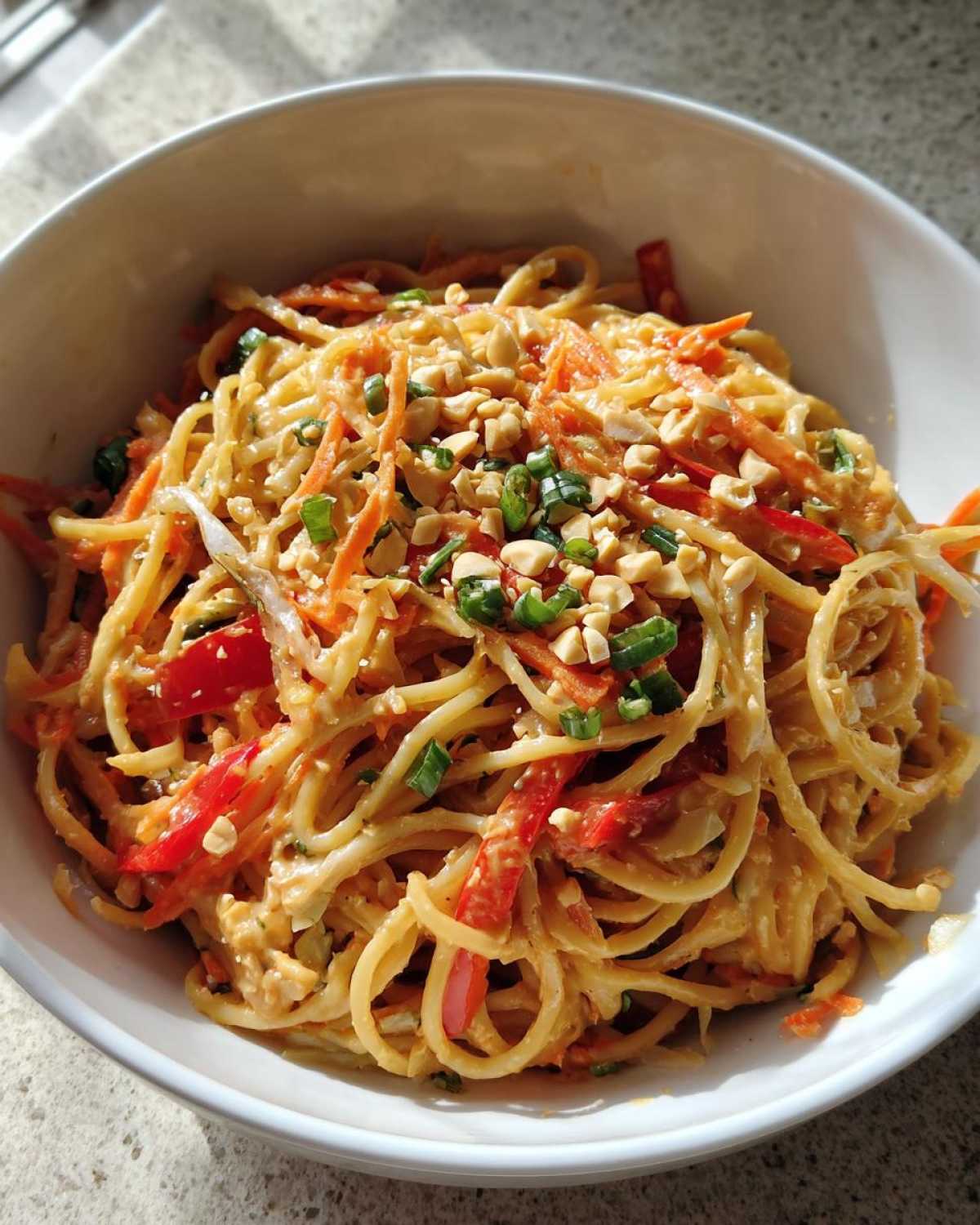 A close-up of Thai Peanut Noodles with Crunchy Veggies, topped with chopped peanuts and green onions.