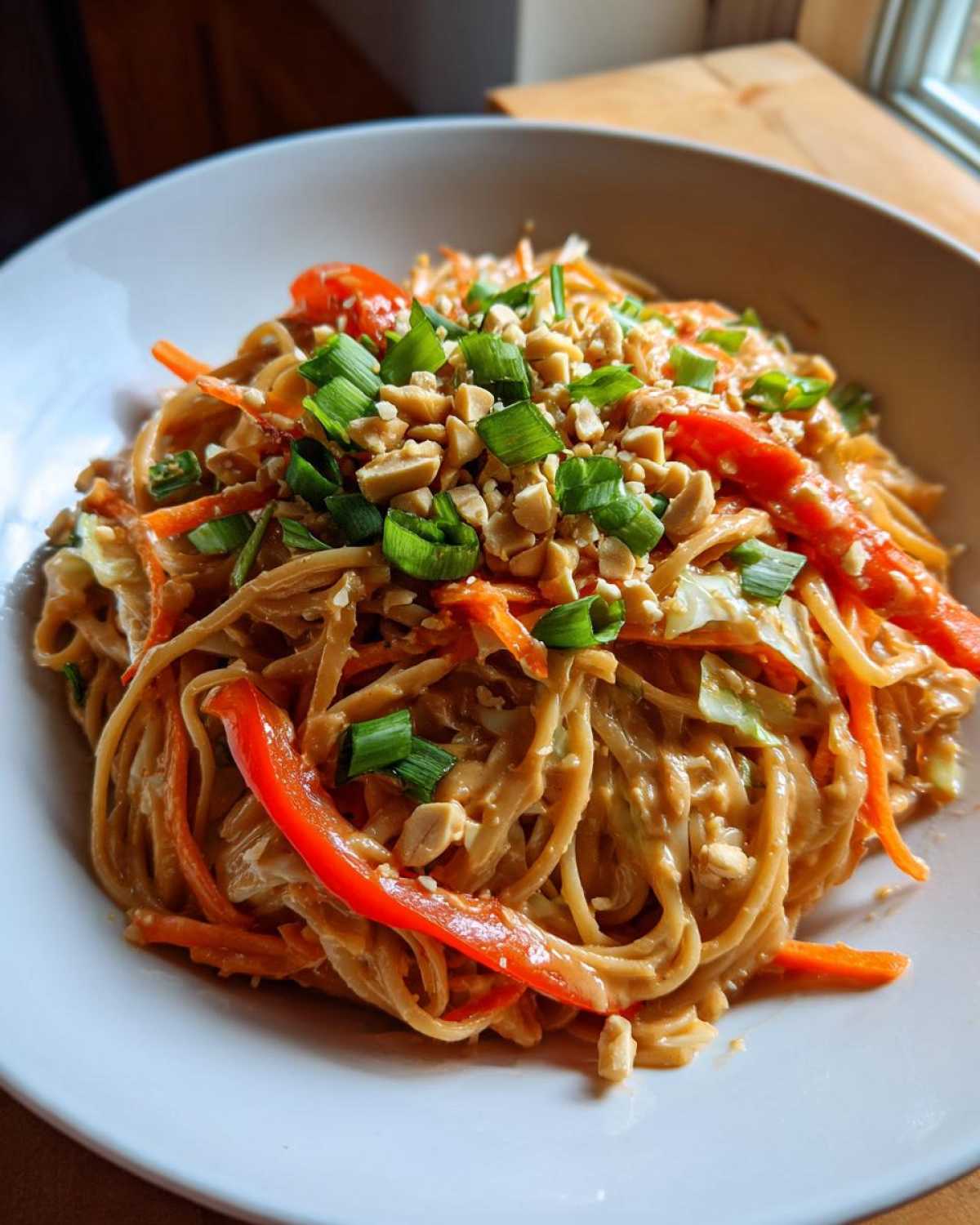 A white bowl filled with creamy Thai Peanut Noodles with Crunchy Veggies, topped with peanuts and green onions.
