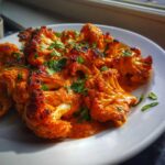 Close-up of roasted cauliflower florets coated in rich orange sauce, part of a Vegan Cauliflower Tikka Masala recipe.