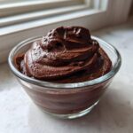 A serving of rich, dark Vegan Chocolate Avocado Mousse swirled high in a small clear glass bowl.