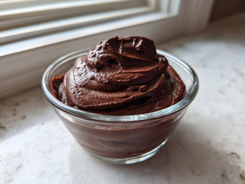 A serving of rich, dark Vegan Chocolate Avocado Mousse swirled high in a small clear glass bowl.