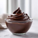 A close-up of rich, dark Vegan Chocolate Avocado Mousse swirled high in a clear glass bowl.