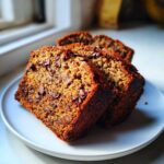 Three thick slices of moist Vegan Chocolate Banana Bread studded with chocolate chips, served on a white plate.