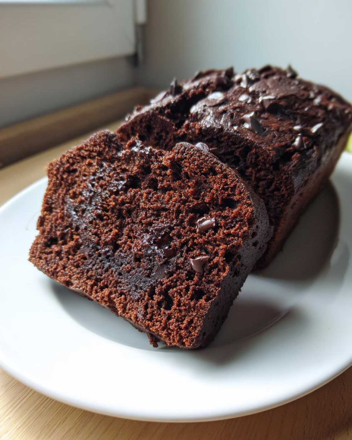 Close-up of moist slices of Vegan Chocolate Banana Bread, topped with chocolate chips, served on a white plate.