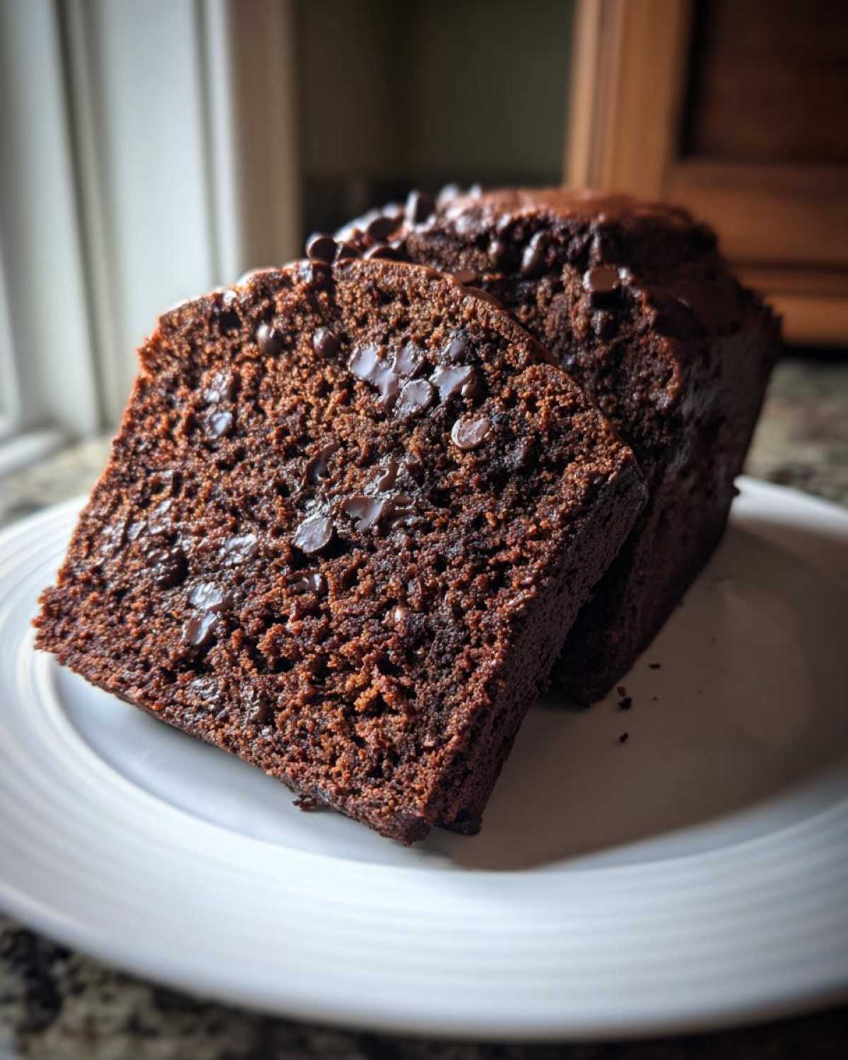 Two moist slices of Vegan Chocolate Banana Bread loaded with chocolate chips, served on a white plate.