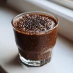 Close-up of thick Vegan Chocolate Chia Pudding in a clear glass, topped with extra chia seeds.