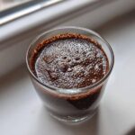 Overhead close-up of rich, dark Vegan Chocolate Chia Pudding with visible hydrated chia seeds in a clear glass.