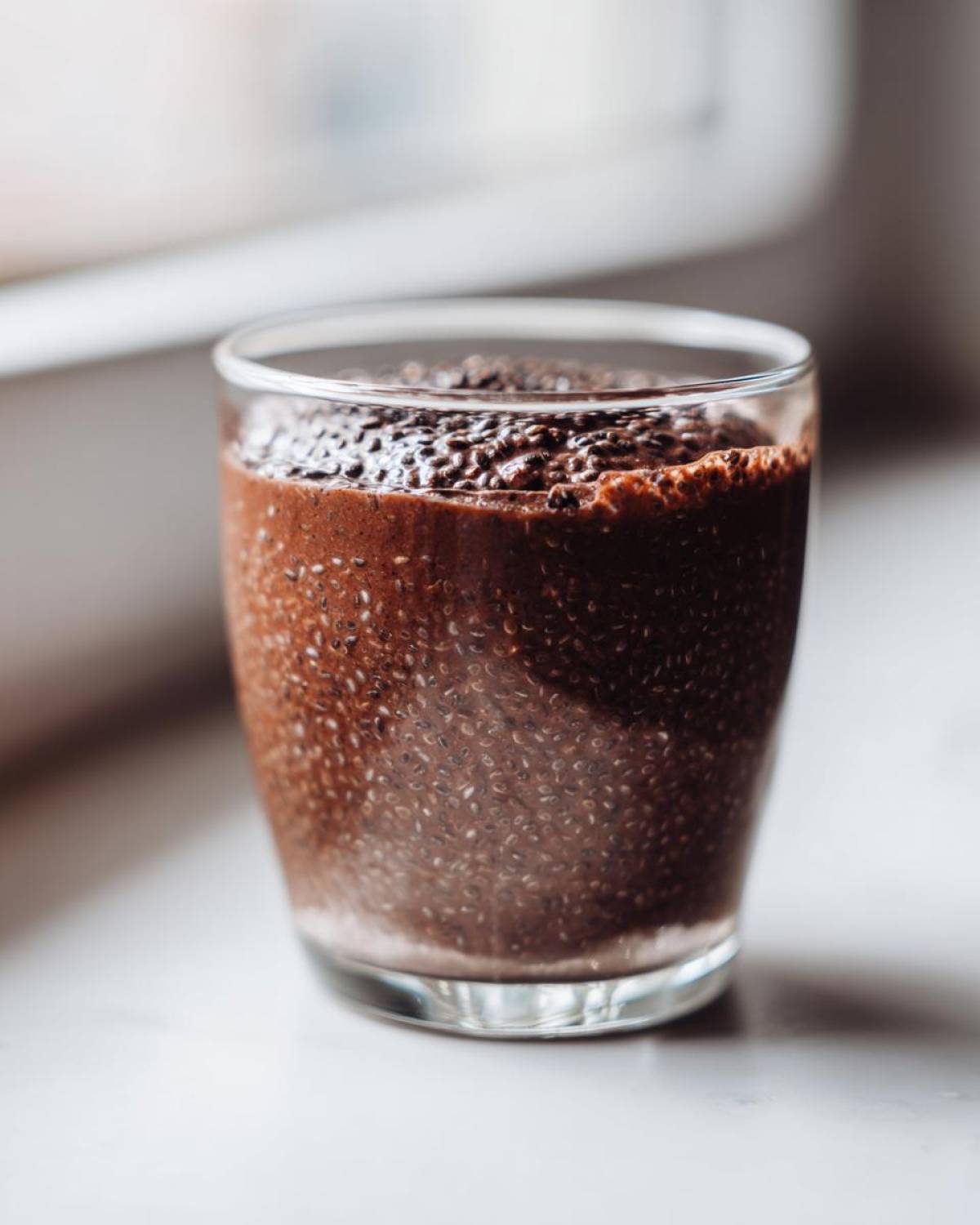 A clear glass filled with thick Vegan Chocolate Chia Pudding, showing the texture of the soaked chia seeds.