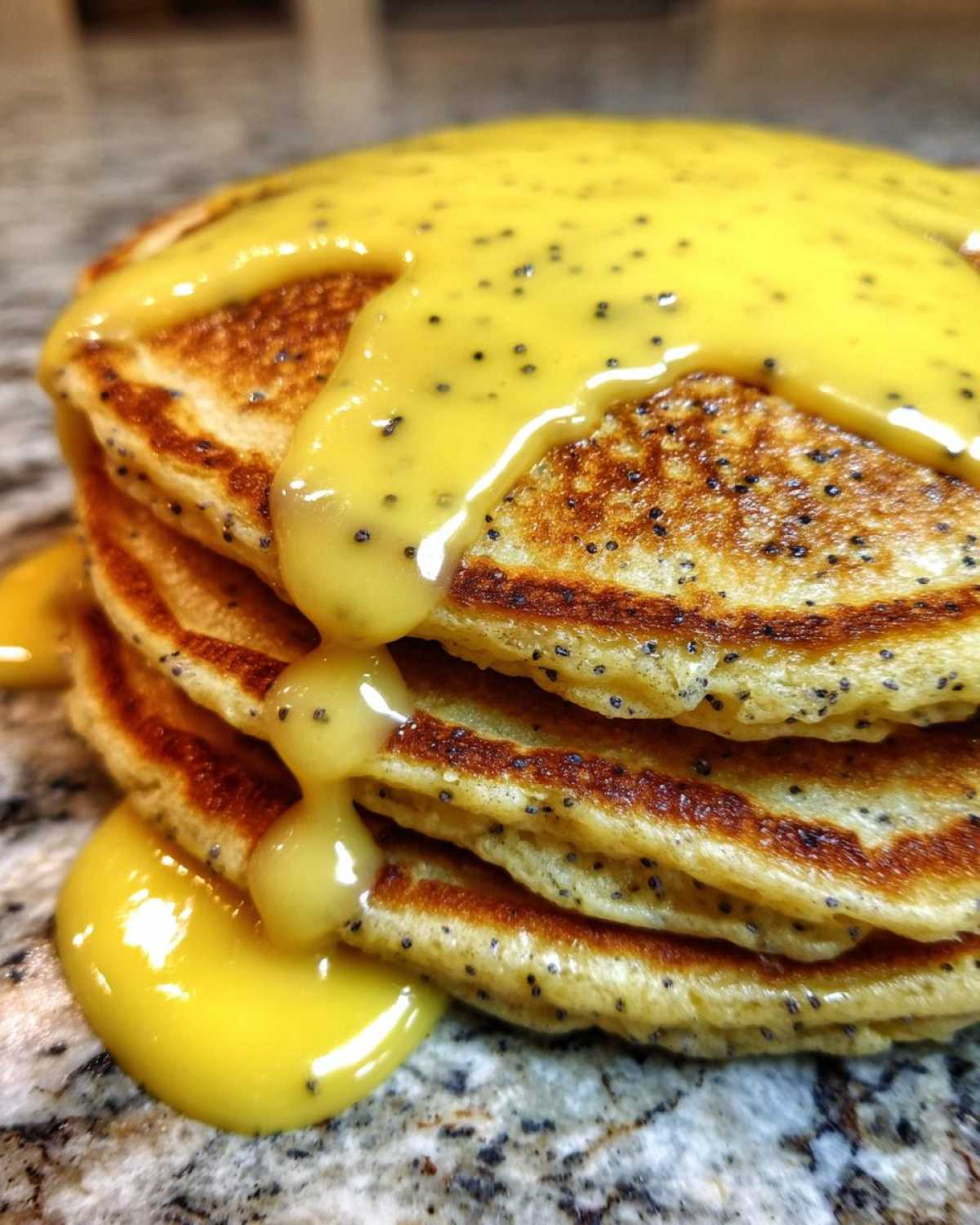 Close-up of a stack of fluffy Vegan Lemon Poppy Seed Pancakes drizzled with bright yellow lemon glaze.
