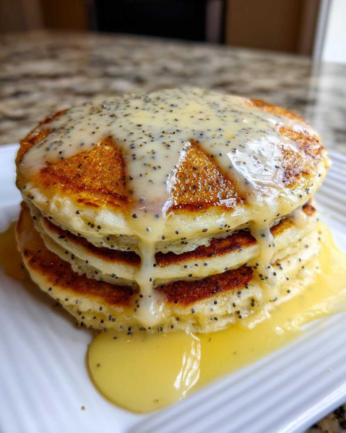 Close-up of a stack of fluffy Vegan Lemon Poppy Seed Pancakes covered in a thick lemon glaze.