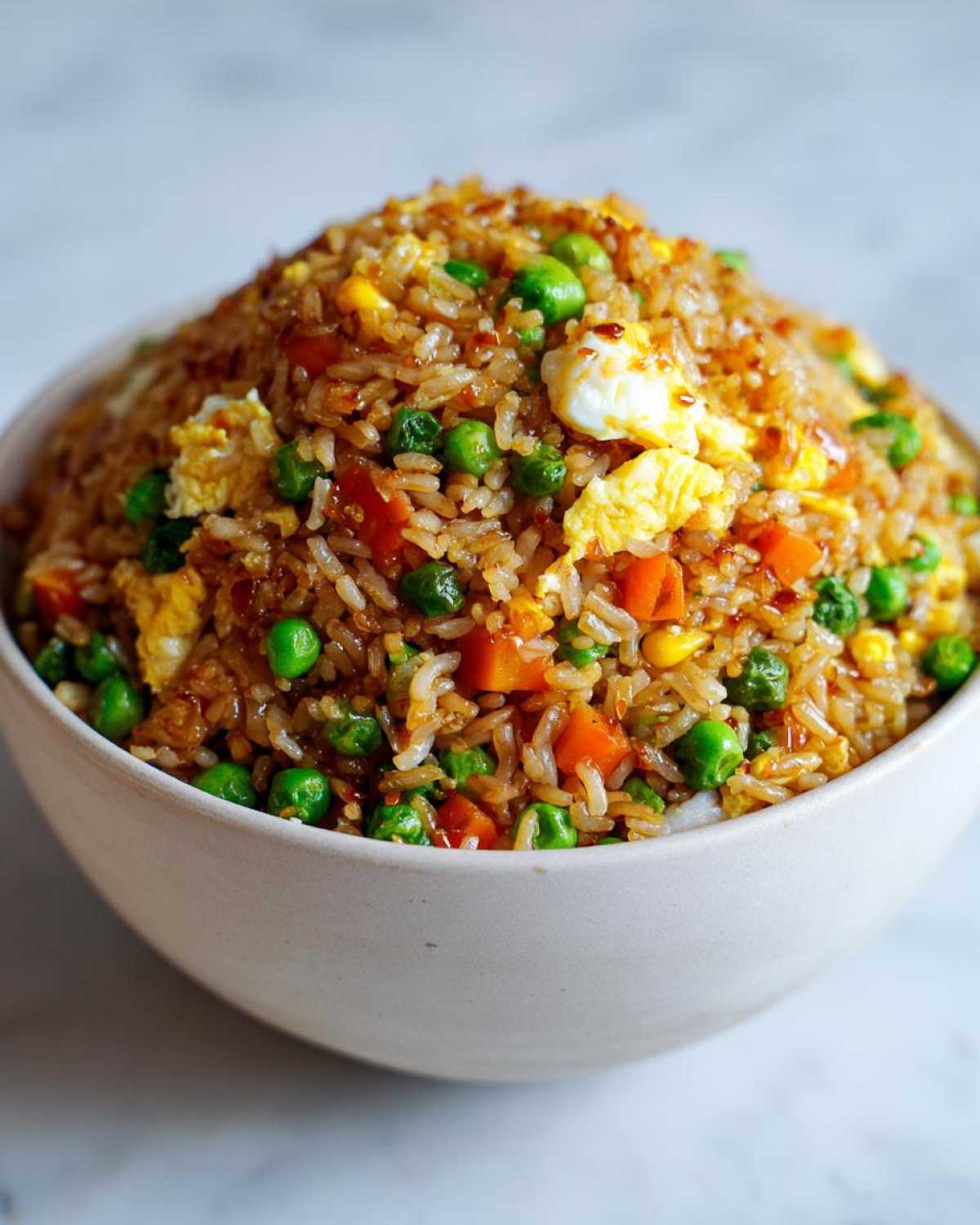 A close-up of a large bowl filled with vibrant Vegetable Fried Rice with Sesame Ginger Sauce, featuring peas, carrots, and scrambled egg.