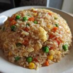 A close-up of a mound of homemade Vegetable Fried Rice with peas, carrots, corn, and scrambled egg on a white plate.
